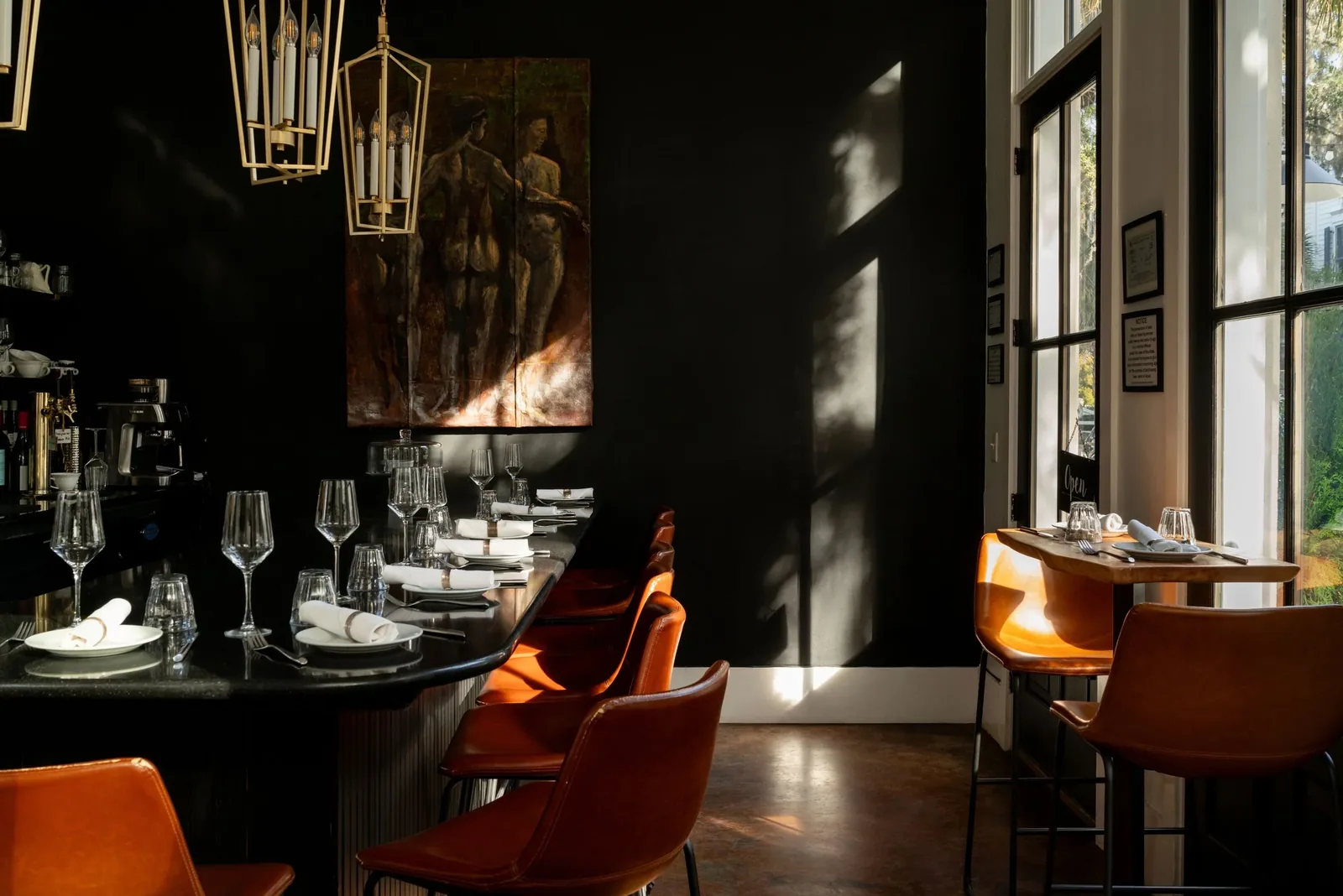 The dining room at Bistro Ten, dark walls and warm lamps with tables set for service