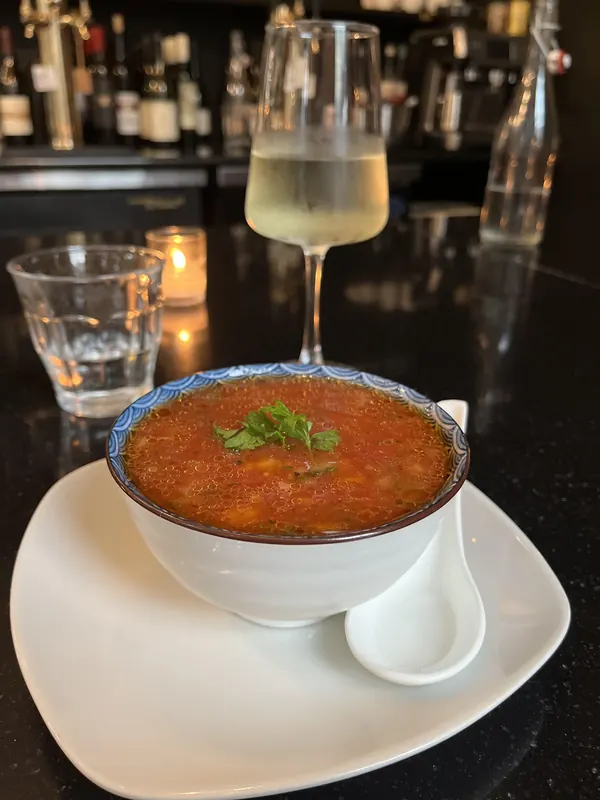 Gazpacho in a blue-rimmed bowl with a glass of white wine