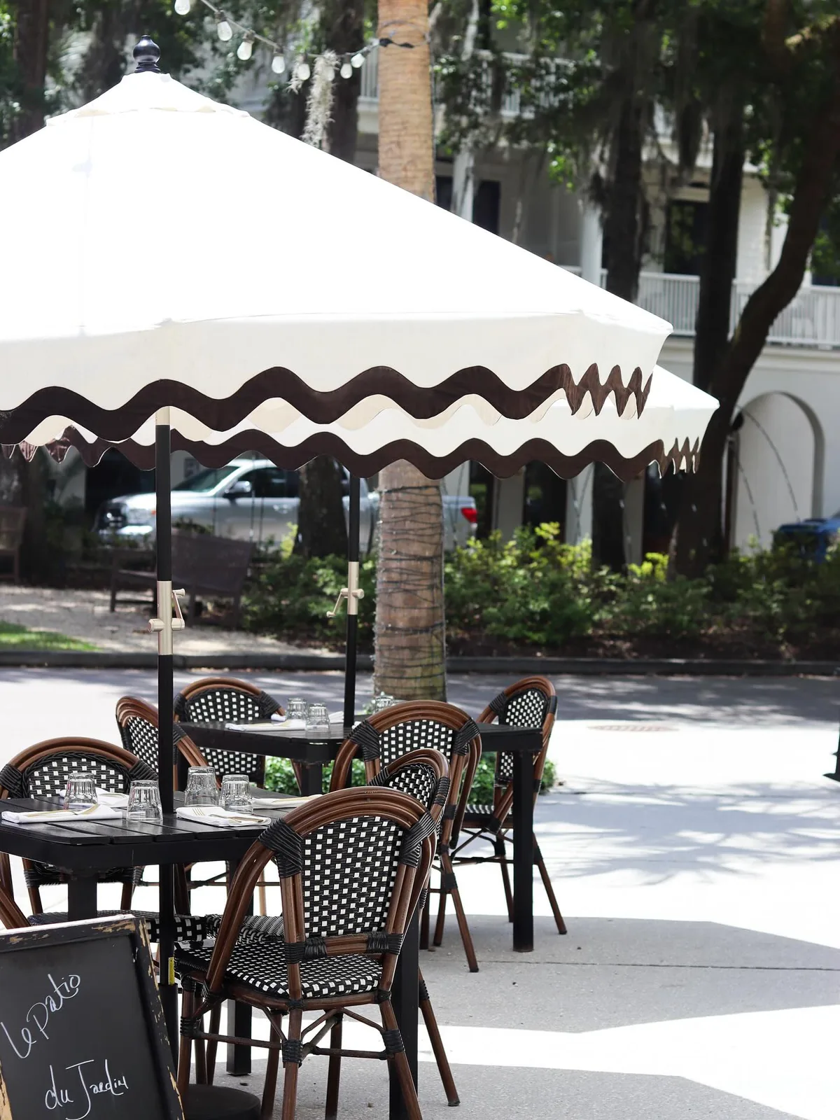 Black bistro tables and woven French chairs on the patio under a rickrack-edged umbrella