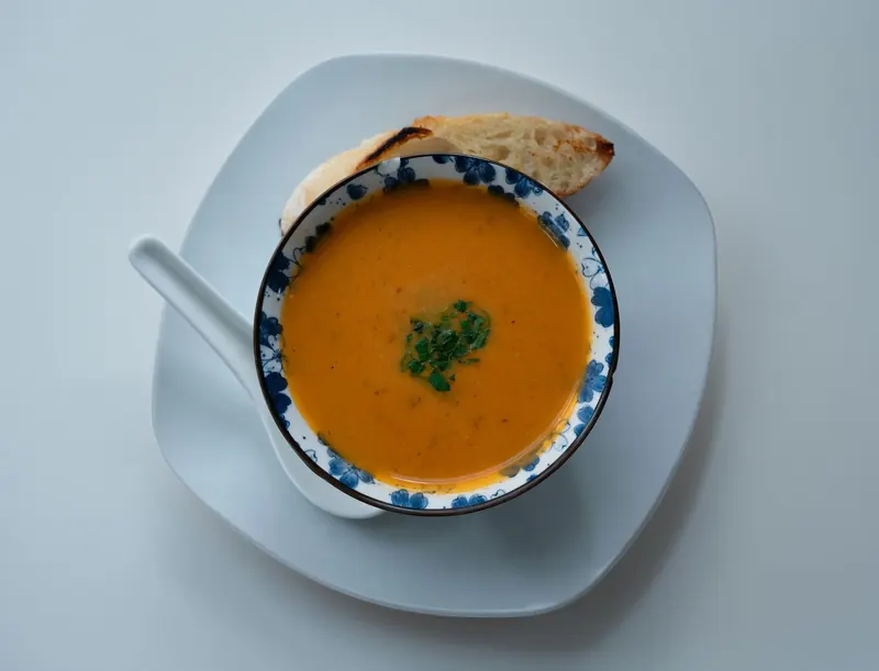 A bowl of soup served with a torn baguette